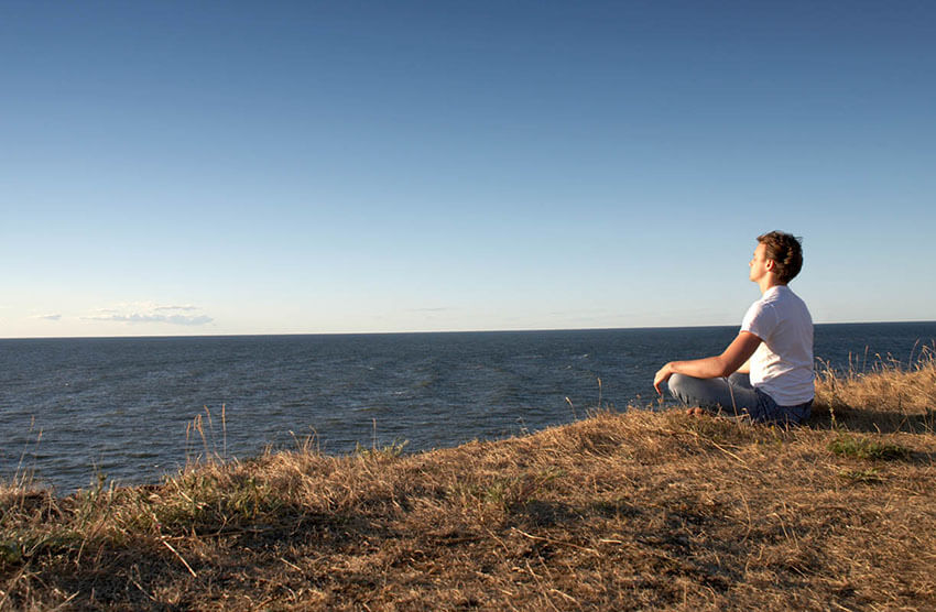 Meditierender sitzt auf einem Hügel vor dem Meer