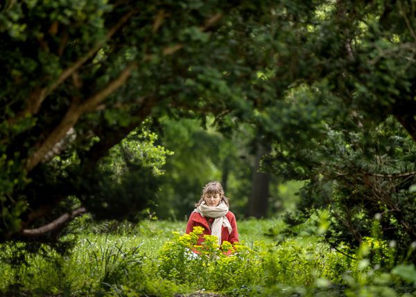 Eine junge Frau sitzt auf einer Wiese umgeben von Bäumen und meditiert